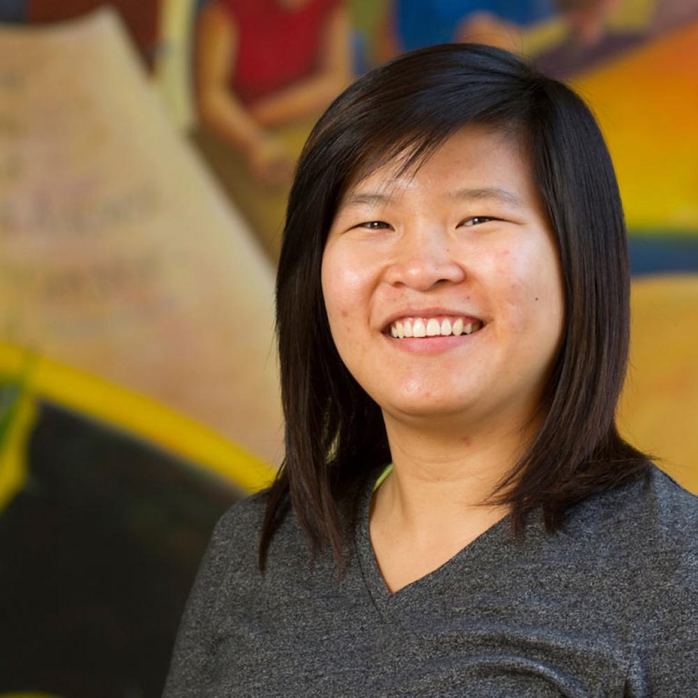 A female student poses in front of a mural 