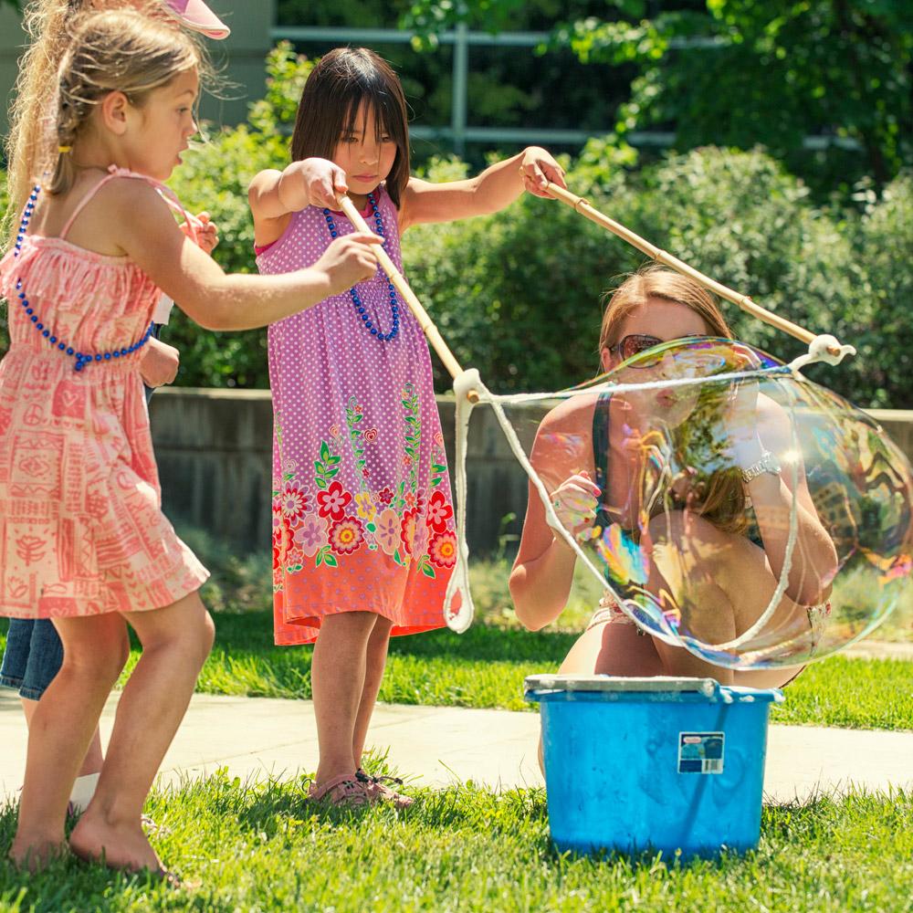 Two children and a parent blowing giant bubbles together