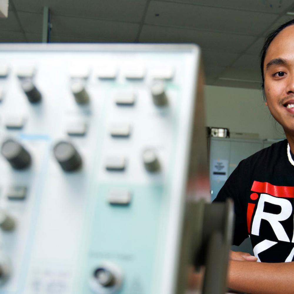 A male student poses next to some engineering lab equipment