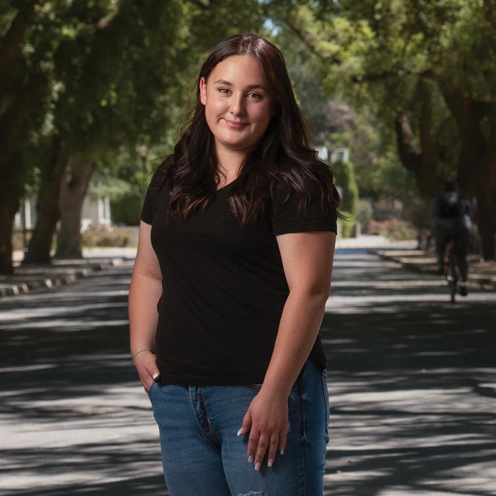 a student stands in front of a road lined with trees on the UC Davis campus