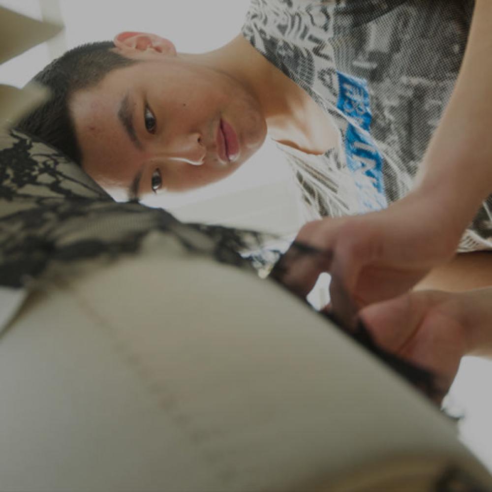 A male student puts the finishing touches on a garment he is designing for the Picnic Day fashion show