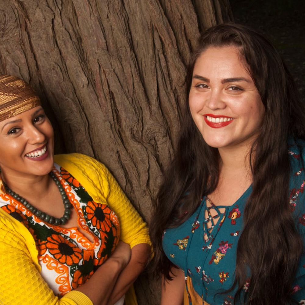 Two women pose in front of one of the oak trees on the UC Davis campus