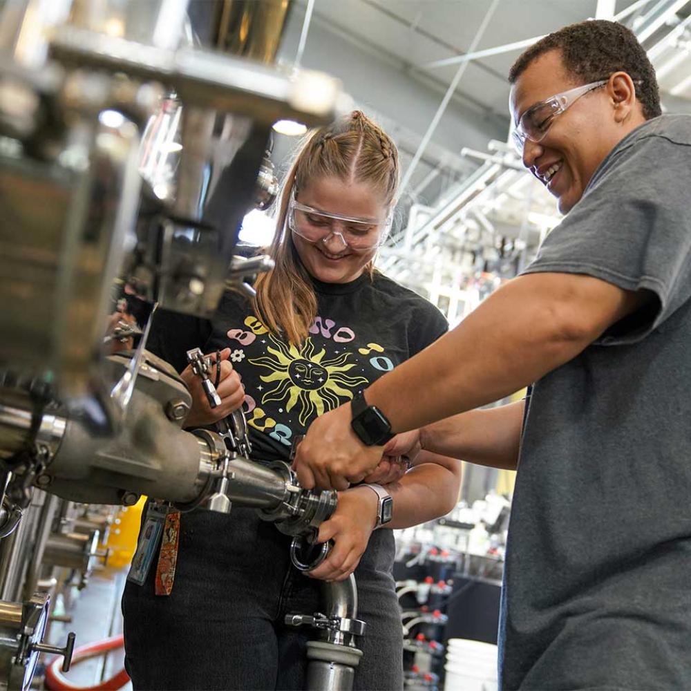 Cameron Rose (female) a senior double majoring in Viticulture and Enology and Managerial Economics and Kyle Williams (male) a senior majoring in Chemical Engineering work together to "rach the lees" in 540 gallon tanks at the winery at the Robert Mondavi Institute for Wine and Food Science.