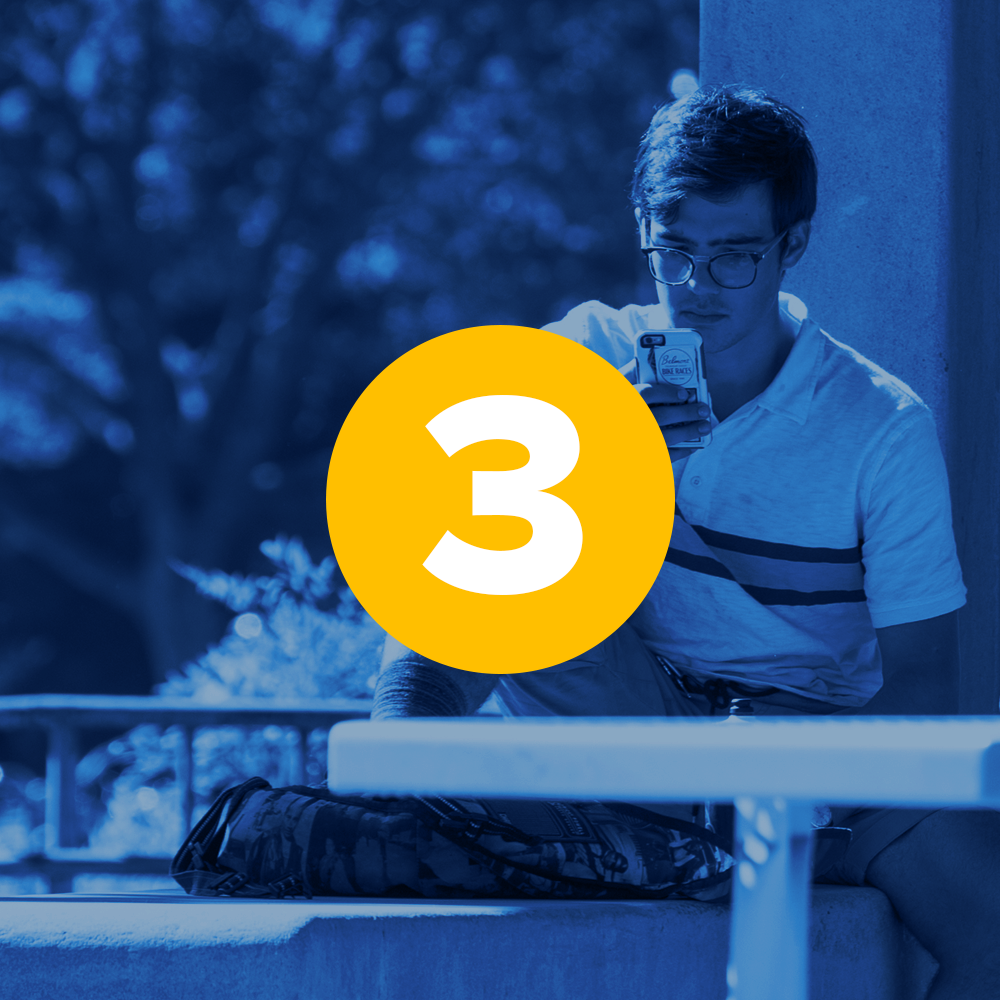 a student sitting outside and looking at a mobile phone