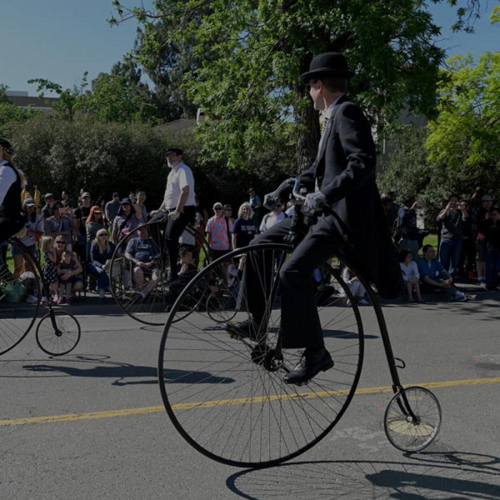 Two people riding penny farthing bicycles through Davis