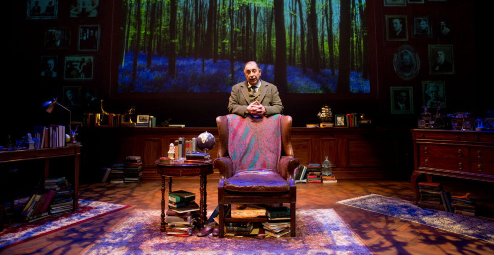 Max McLean as C.S Lewis standing behind an upholstered chair in Lewis' study.