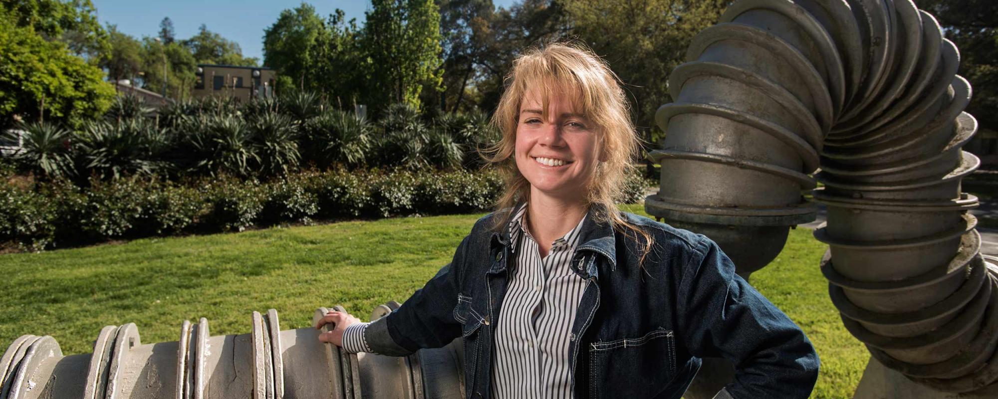 Art lecturer May Wilson posing in front of a metal sculpture