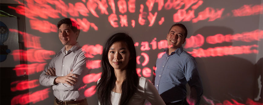 Three people stand amid the projection of red computer code