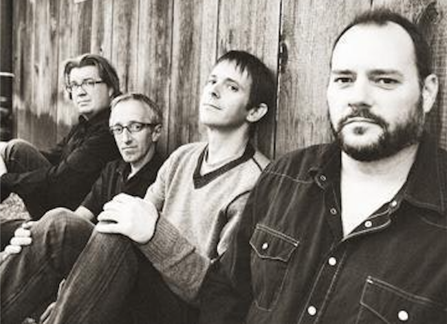 A photo of the band members sitting on the ground and leaning against a wall.