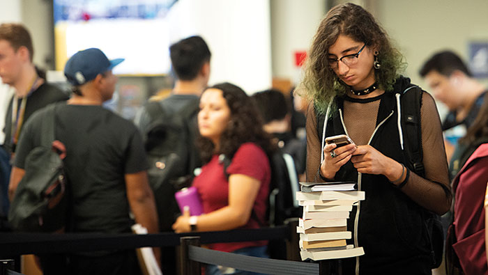 Alyxx Melendez checks prices on books while waiting in line