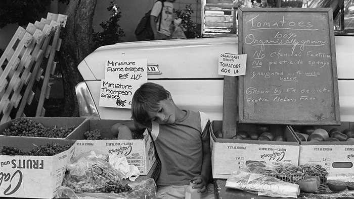 A young merchant rests his eyes at a produce stand at the Davis Farmers Market