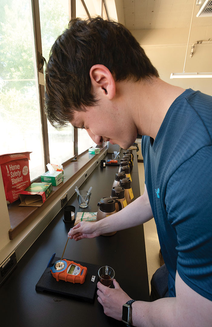 A student watches as they pipette drops of coffee on to an electronic lab instrument's sensor.