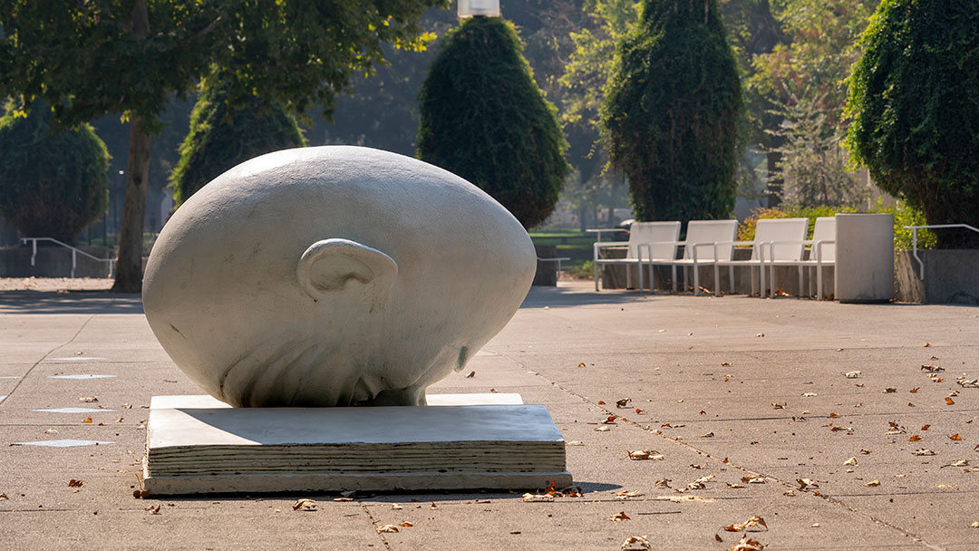The Bookhead Egghead sculpture with the library plaza in the background on a sunny day.