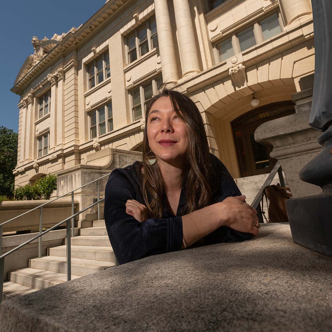 A woman stands on the steps outside the front of Sacramento City Hall and looks off camera. She is wearing a black blazer.